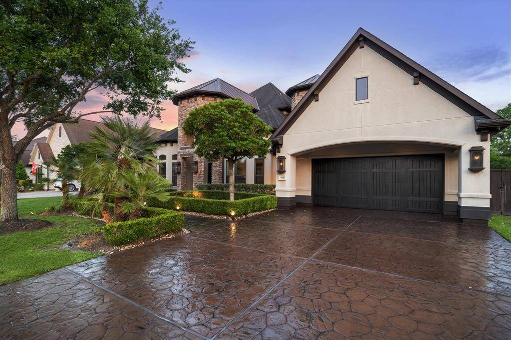 The residence boasts a blend of stone and stucco finishes, accented by striking rooflines and dark architectural shingles for a timeless European-inspired aesthetic. The extra-wide stamped concrete driveway offers ample parking and leads to a spacious 3-car tandem garage with a rich, dark wood carriage-style door. Inside the garage, premium features await, including finished floors, insulated walls, a convenient side door to the backyard, and an automatic garage door opener.