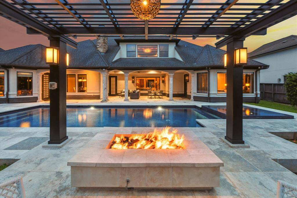 This stunning outdoor oasis delivers resort-style living at its finest. Centered around a luxurious pool and elevated infinity spa, the space is framed by a covered patio and expansive travertine deck—ideal for lounging or entertaining. A sleek fire pit beneath a contemporary pergola invites cozy evenings under the stars, while ambient lighting sets the mood. With seamless indoor-outdoor flow, this private retreat elevates both relaxation and entertaining in effortless style.