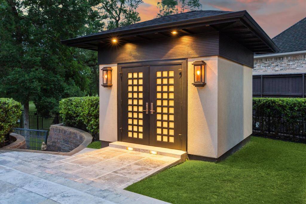 This serene Zen-inspired pool house serves as a tranquil extension of the outdoor living space, thoughtfully designed to offer both form and function. Featuring a contemporary double-door entry flanked by warm gas sconces, it houses a convenient full bathroom and dressing room completing the resort-style ambiance of the backyard oasis. Also, note the stone stairway and iron gate leading to the creekfront property and greenspace behind the home.
