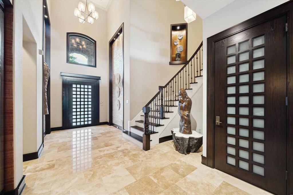 From the moment you step inside, this stunning foyer blends architectural elegance with curated design. The open layout is accented by lighted art niches, a curved staircase with wrought iron spindles, and a curved inset perfect for showcasing a sculptural centerpiece that adds gallery-like elegance. Thoughtful architectural lighting highlights the textures and finishes throughout, while an upper gallery and large arched window invite natural light into this truly unforgettable space.
