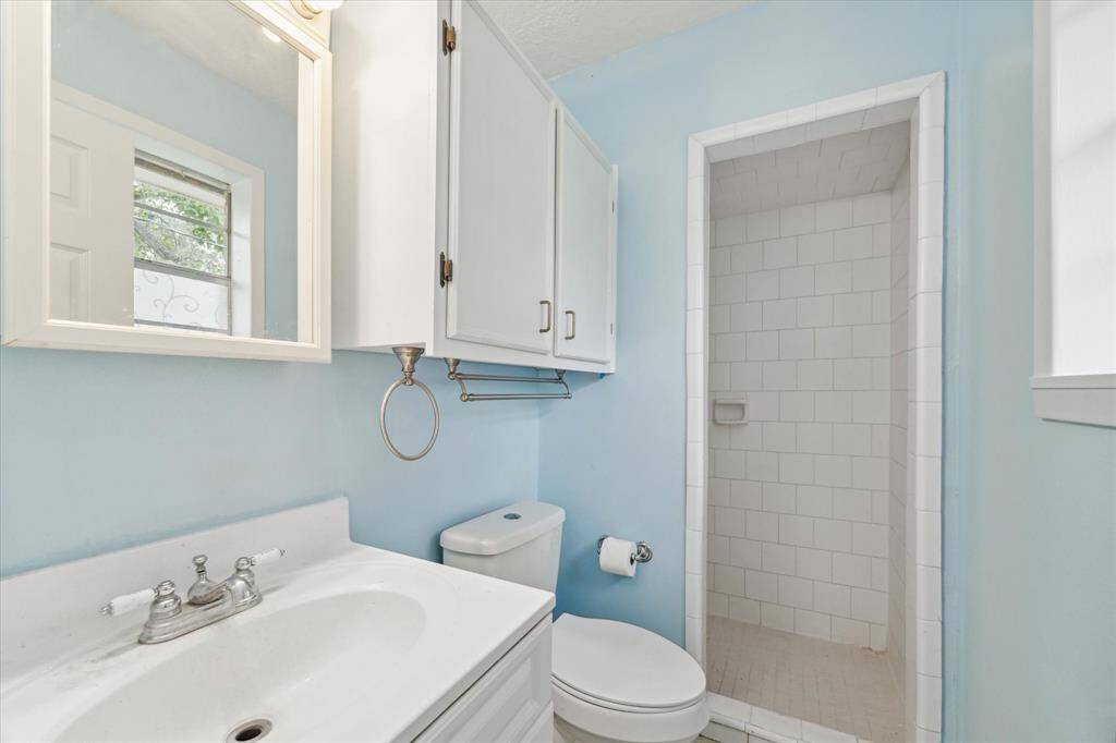 This is a bright, empty room featuring light blue walls, modern grey laminate flooring, and a ceiling fan. There's ample natural light from a large window, and the room includes built-in closets for storage.
