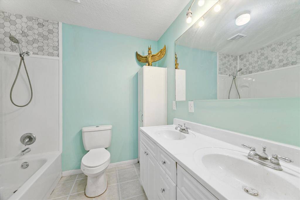 This is a bright, spacious room with yellow walls, modern gray wood-look flooring, and two large windows providing ample natural light. It also features a ceiling fan with a light fixture.