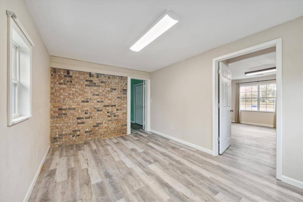 This is a bright, empty room with mint green walls and modern gray wood-look flooring. It features a ceiling fan and a window that brings in natural light. The room opens to another area, suggesting a flowing floor plan.