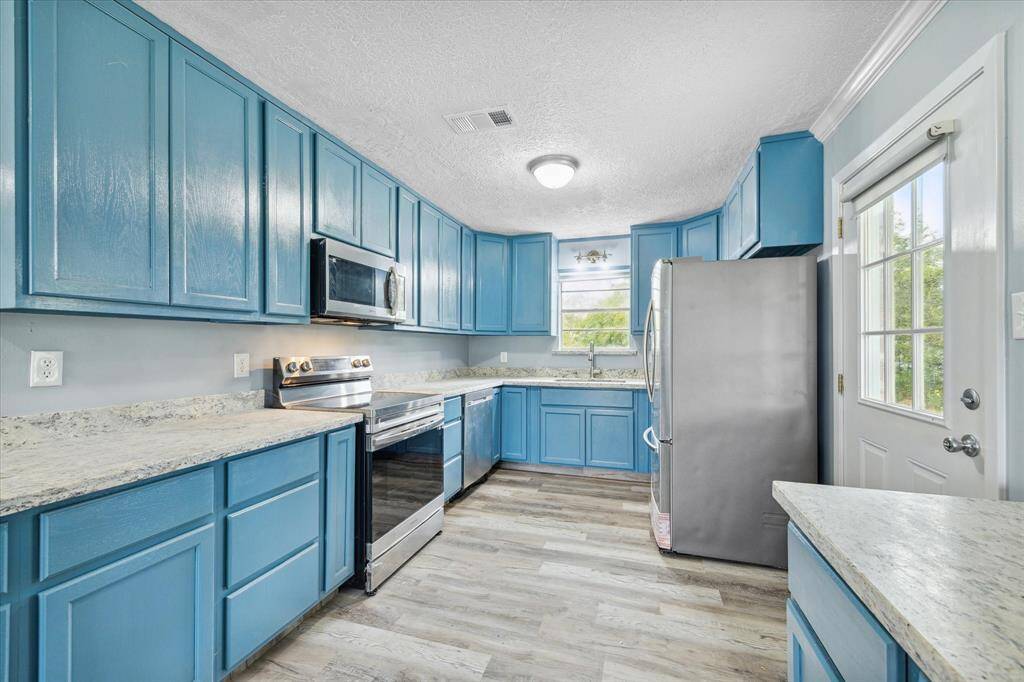 This is a spacious, open-plan living area with contemporary gray walls and wood-look flooring. It features a ceiling fan, ample natural light, and a kitchen bar counter.