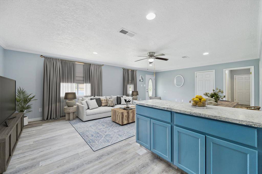 This is a bright, updated kitchen with modern blue cabinetry, ample counter space, sleek appliances, and a view to the outdoors through large windows. The room features wood-look flooring and a fresh, neutral color scheme.