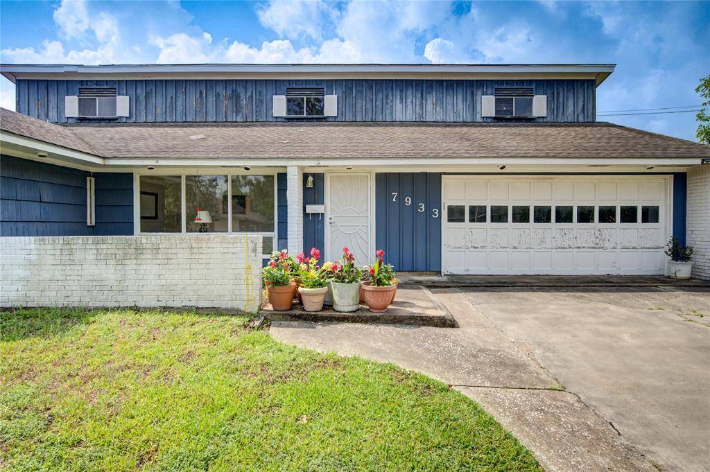 Charming one story home with a blue and white exterior, featuring a spacious driveway and a car garage. The front yard includes a small garden area with potted plants, adding a touch of greenery. Large windows offer natural light and a welcoming entrance.