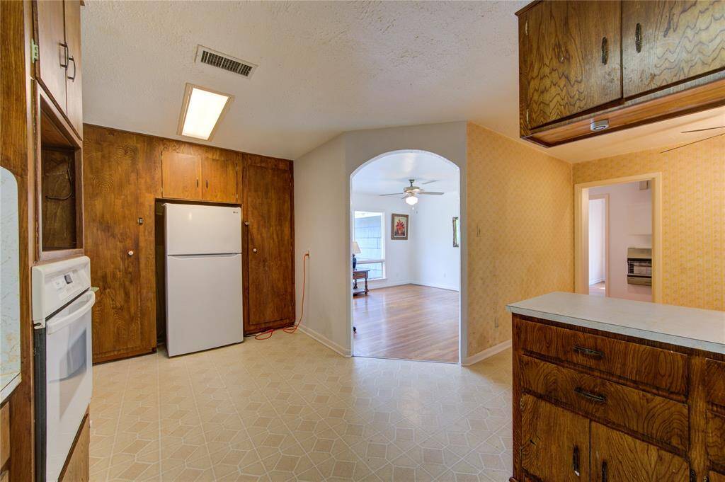 This kitchen features vintage wood cabinetry and a white appliance set, opening to a living area with hardwood floors and ceiling fan, creating a cozy, functional space.