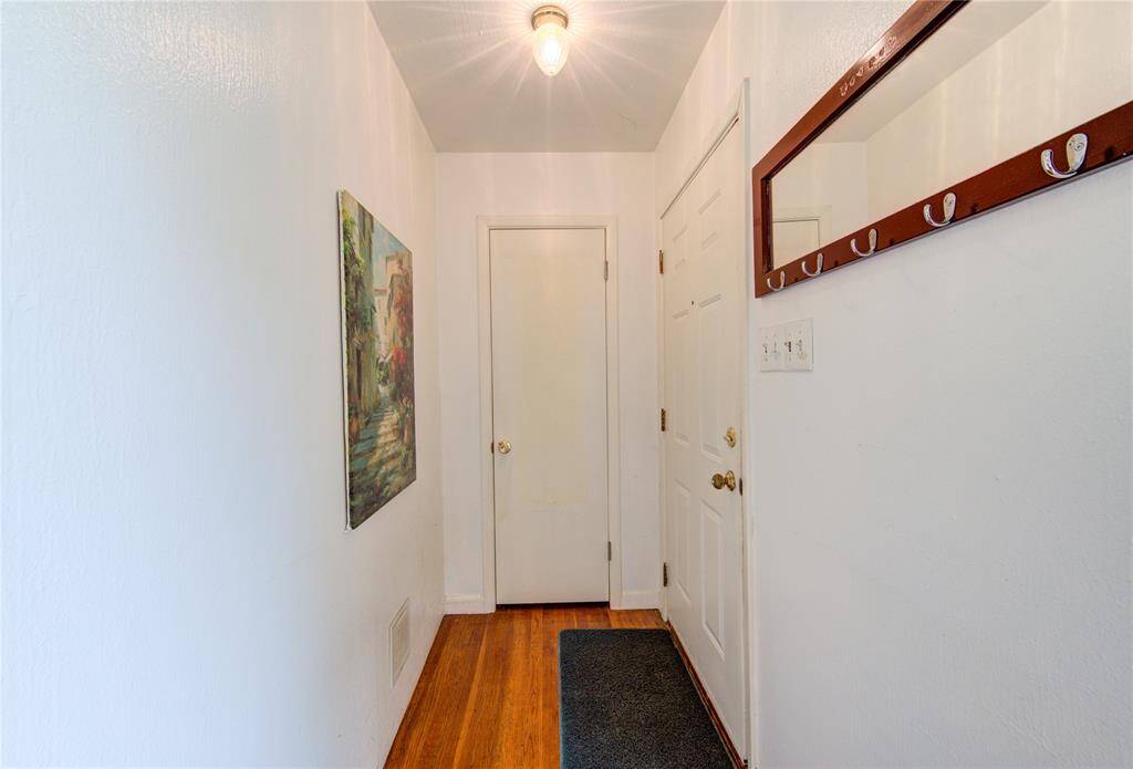 This entryway features hardwood floors, a simple light fixture, and a coat rack. The white walls provide a clean look, complemented by an artistic wall painting.