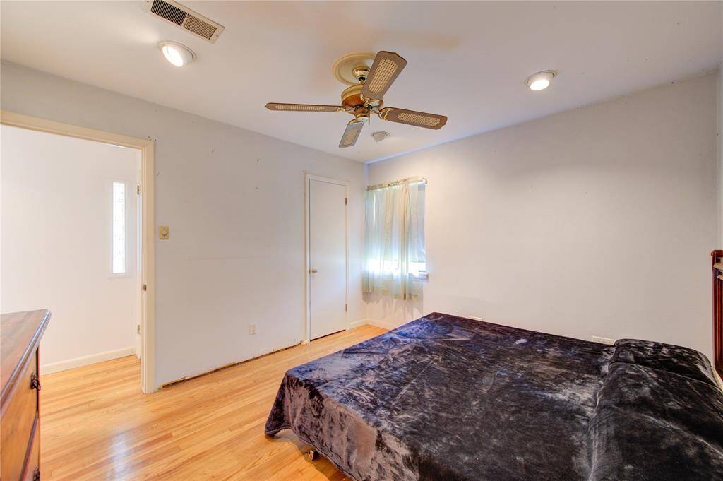 This bedroom features hardwood floors, a ceiling fan, and recessed lighting. It has a window with curtains for natural light and an adjacent doorway leading to another room.
