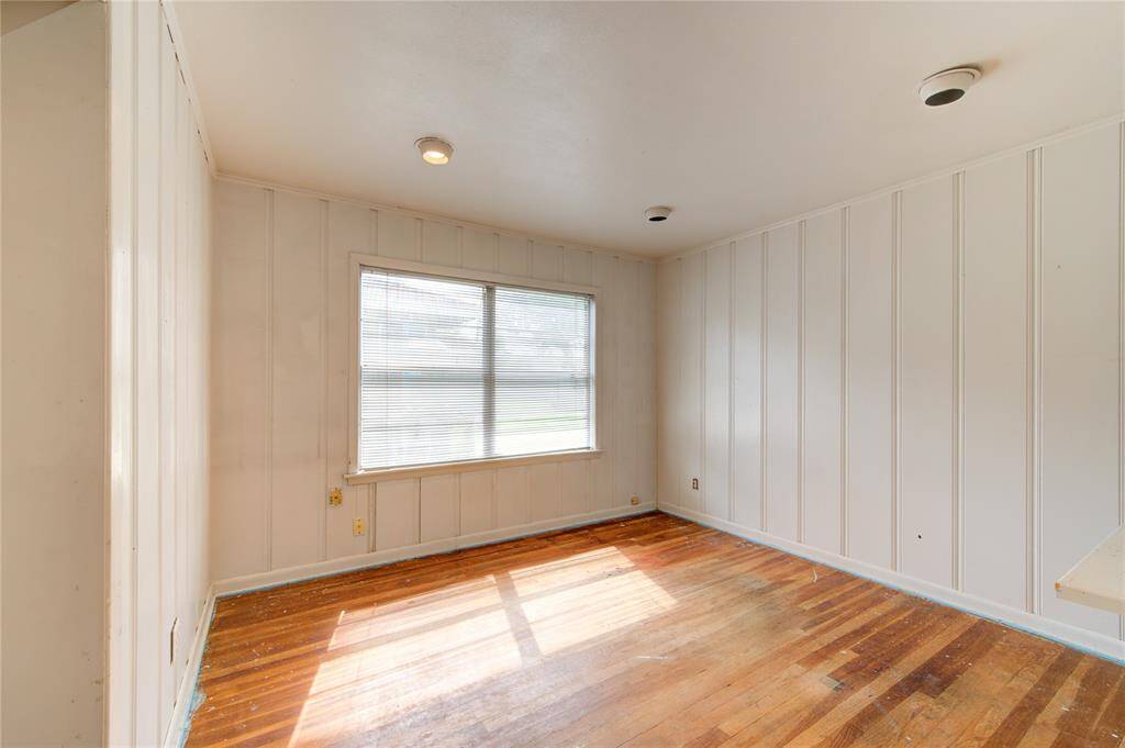 Bright room with wood flooring, paneled walls, and a large window allowing natural light. Ideal for an office or cozy living space.