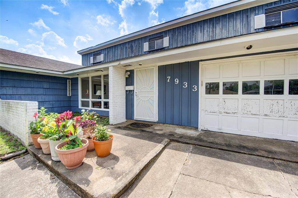 This charming home features a classic exterior with blue siding and white accents. The welcoming entrance includes a secure metal screen door. A small garden with colorful potted plants adds curb appeal.