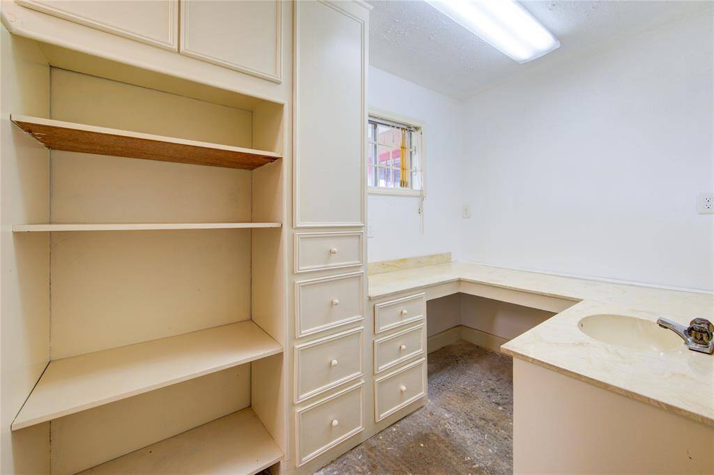 This room features built-in shelving and cabinetry with a small window providing natural light. It includes a countertop space with a sink, ideal for a utility or laundry room. The lighting is bright, and the floor appears unfinished.