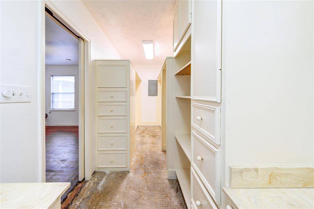 This photo shows a walk-in closet with ample built-in shelving and drawers, featuring a neutral color scheme. It leads into a room with natural light from a window, and the flooring appears unfinished.