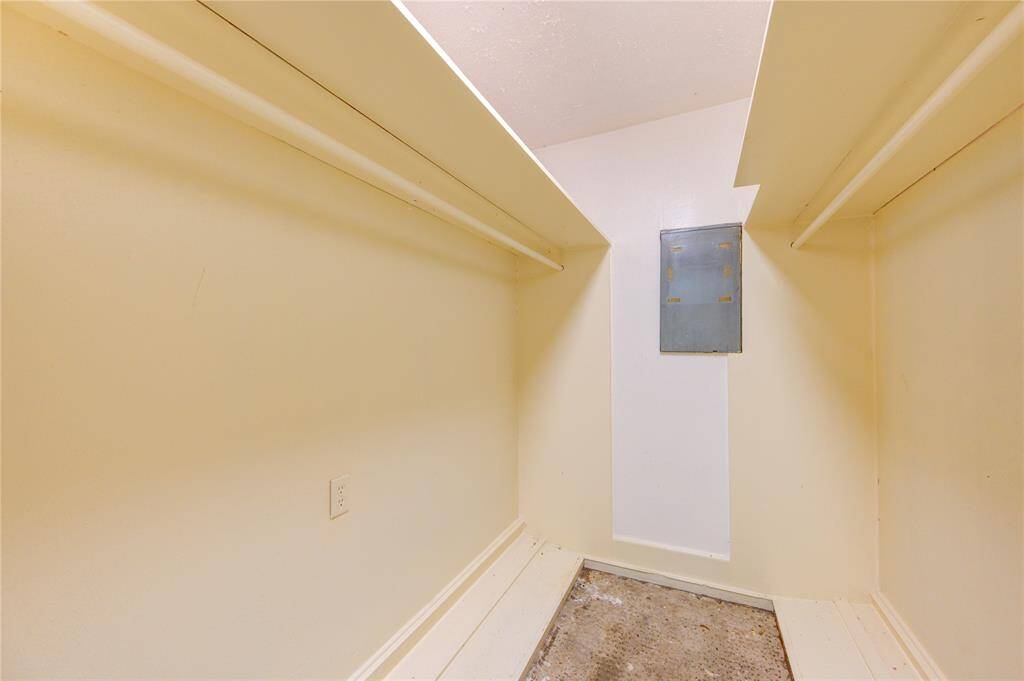 This photo shows a small walk-in closet with hanging rods on both sides, a neutral color scheme, and a utility panel on the back wall. Ideal for organized storage.
