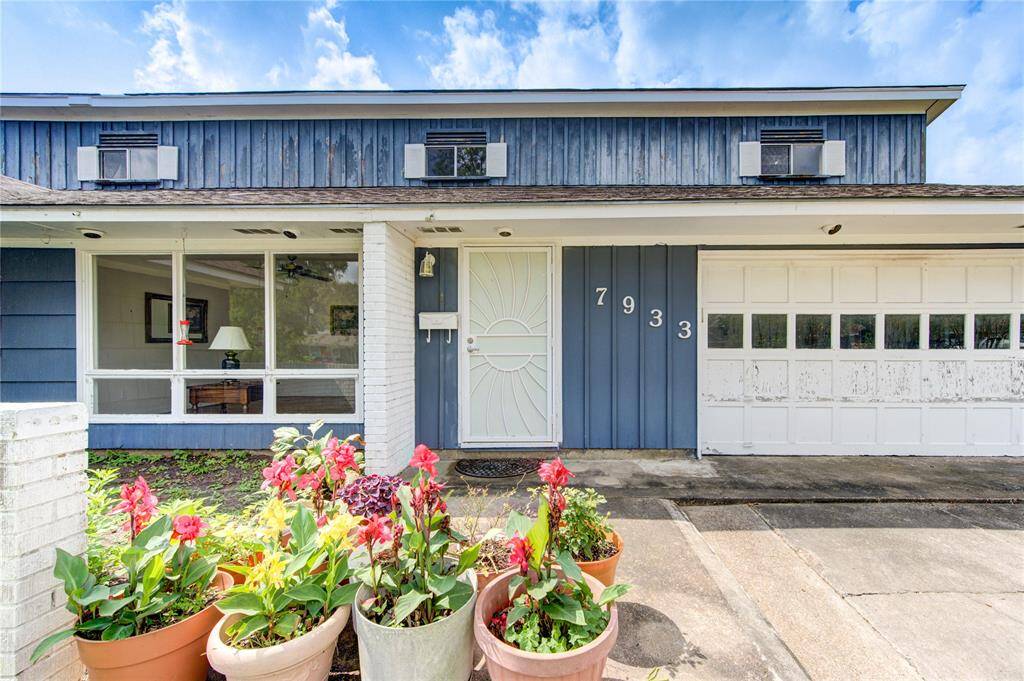 The house features a welcoming front entrance, large window, and an attached garage. The front yard is adorned with vibrant potted flowers, adding a touch of color and appeal.