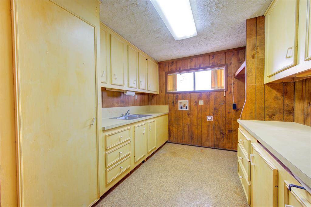 Cozy kitchen with a retro feel, featuring wood paneling and ample cabinetry. It has a basic countertop space and a window providing natural light.