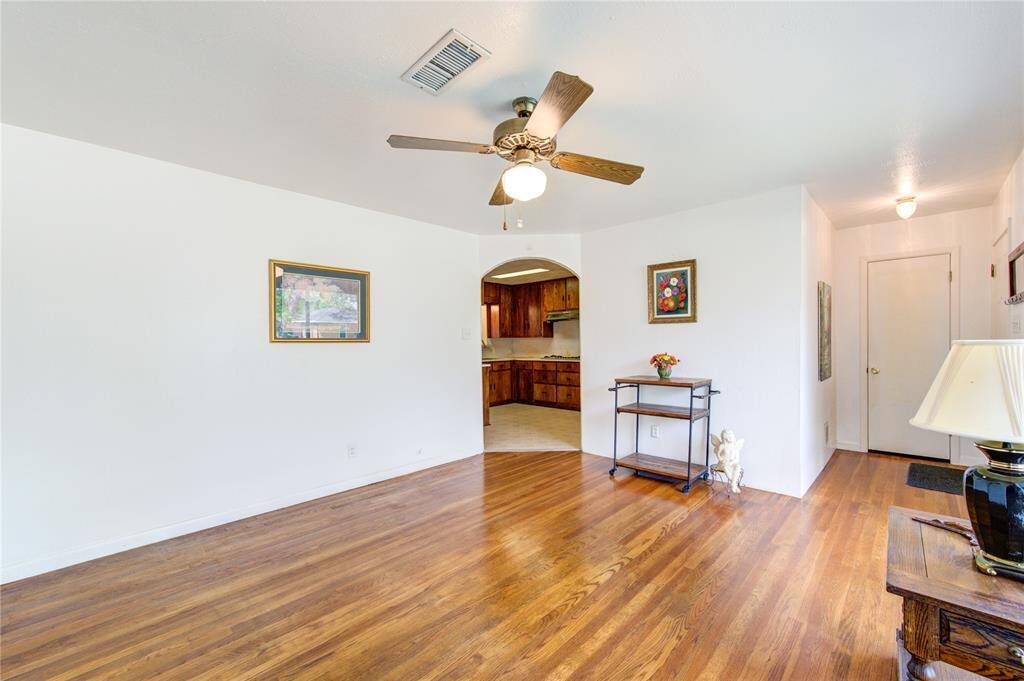 Bright living area with wood floors, a ceiling fan, and neutral walls. The space connects to a kitchen through an arched doorway, offering a warm and welcoming feel.