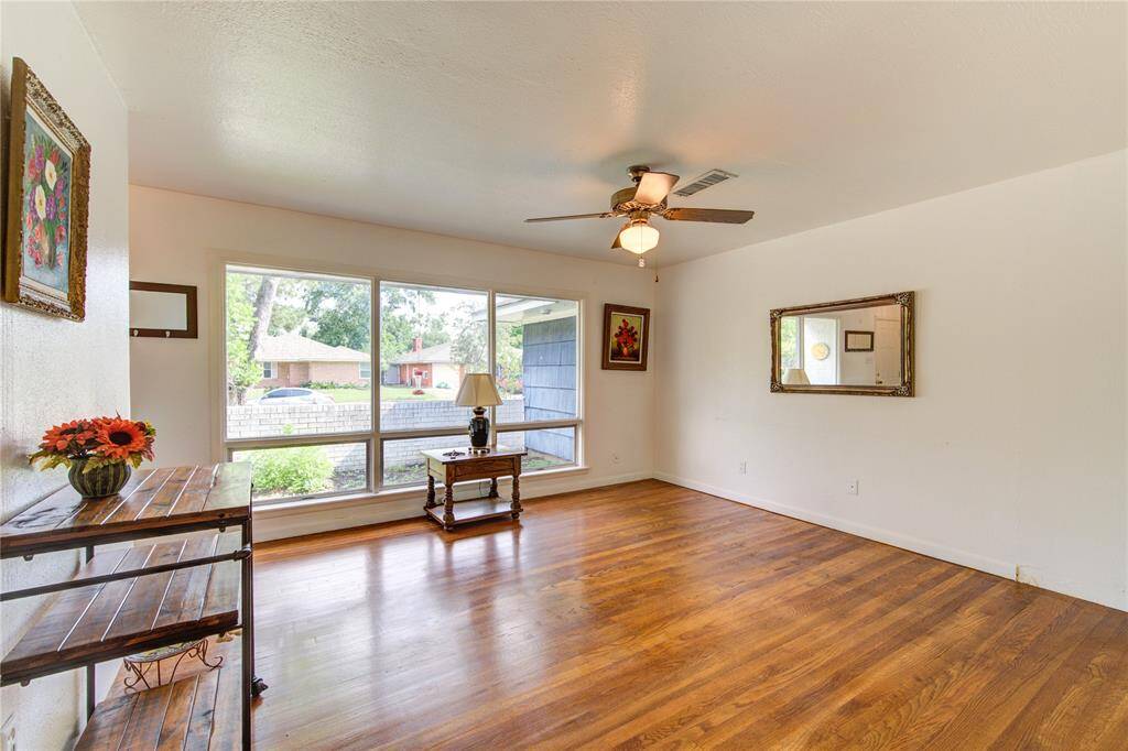 Bright living room with large windows, hardwood floors, and a ceiling fan. The room is minimally decorated with a mirror, artwork, and a small side table.