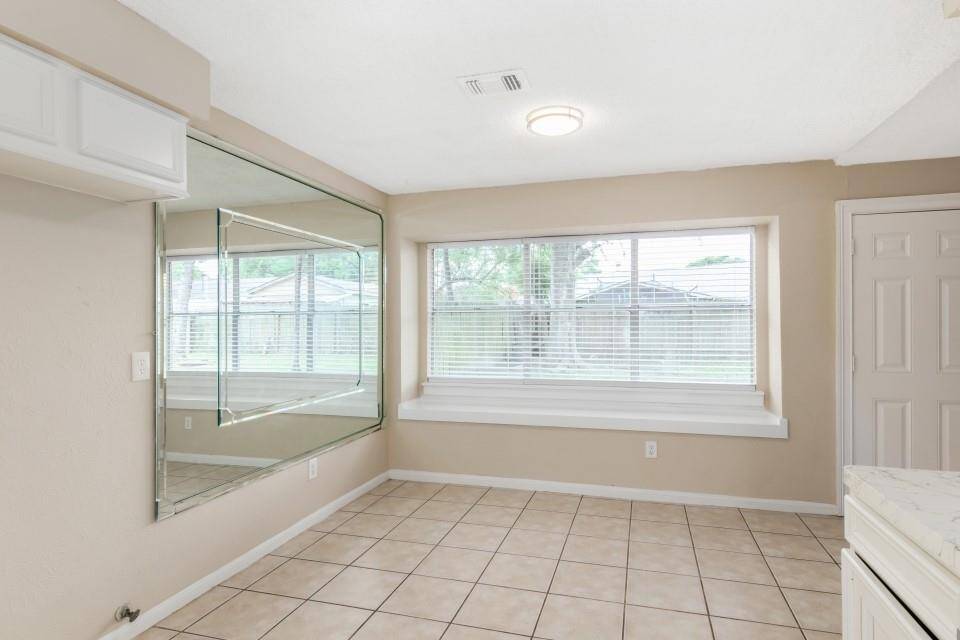 Bright room with large windows, tiled floors, and a mirrored wall, providing a spacious feel. Ideal for a dining or sitting area.