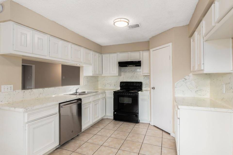 This kitchen features white cabinetry, marble-style countertops, a black stove, and stainless steel dishwasher. The tile flooring complements the neutral wall color, creating a bright and modern space.