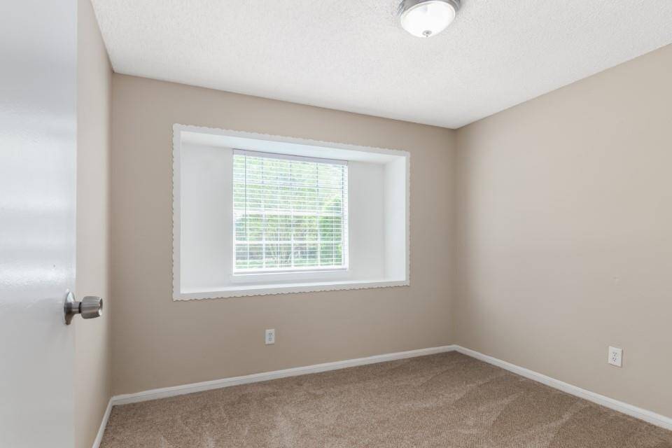 This is a small, carpeted room with neutral-colored walls, featuring a large window that lets in natural light. Ideal for a bedroom or home office.