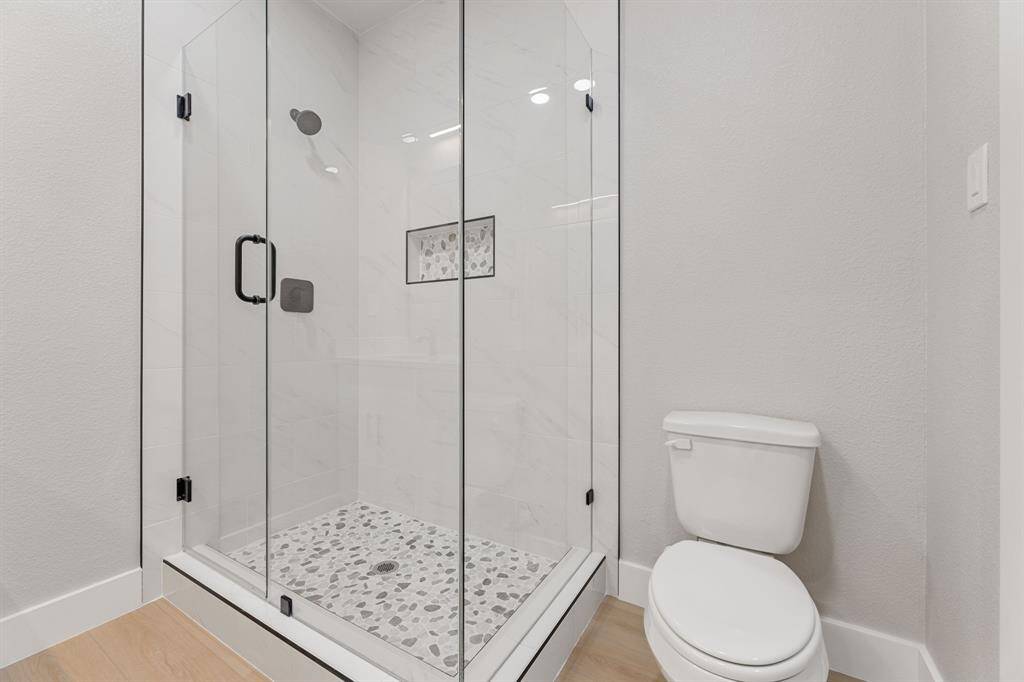 A spa-like experience awaits. This beautifully designed walk-in shower features elegant marble-look tile, a stylish pebble stone floor, and sleek black fixtures—perfect for unwinding in a modern, tranquil space. The clean, frameless glass doors add a touch of sophistication to your primary bath.