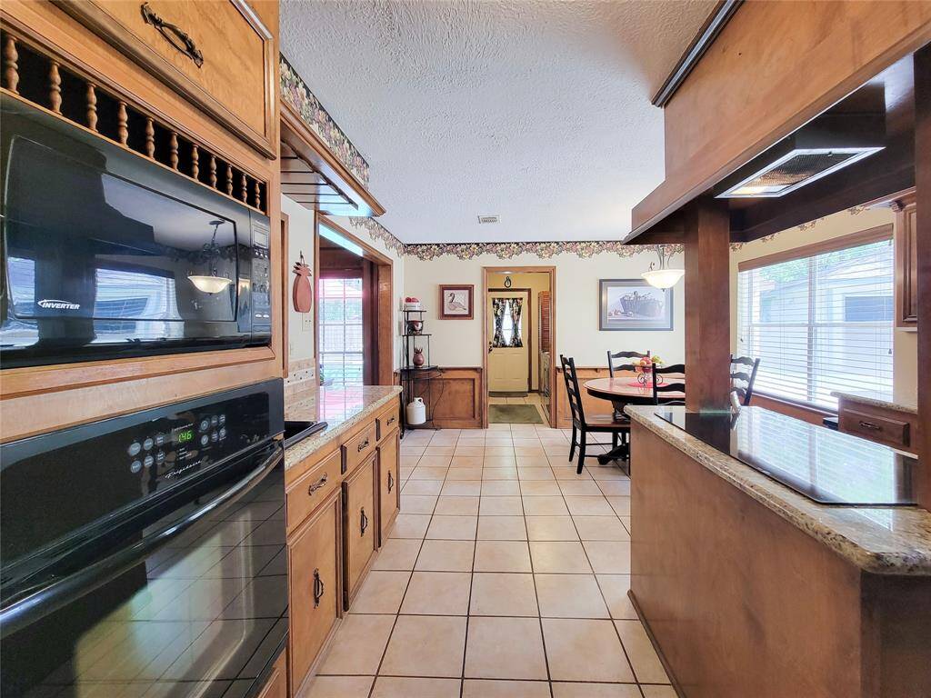 This kitchen features warm wood cabinetry, tiled flooring, and ample natural light. It includes a built-in oven, a cozy dining area, and decorative trim, creating a welcoming and functional space.