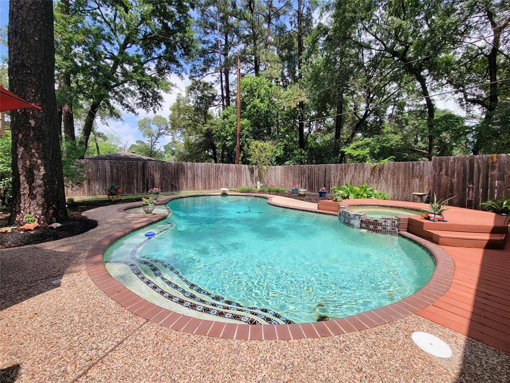 This photo showcases a serene backyard with a kidney-shaped pool, surrounded by lush greenery and tall trees. The area features a wooden deck, a hot tub, and a privacy fence, creating a perfect retreat for relaxation.