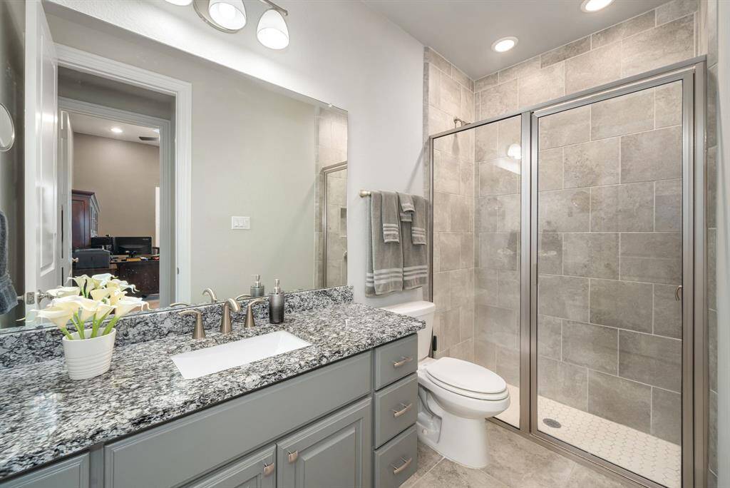 A full bath on the 1st floor across from one of the secondary bedrooms. This well-appointed bathroom has a lovely tiled stand-up shower, a long granite countertop, and lots of storage.