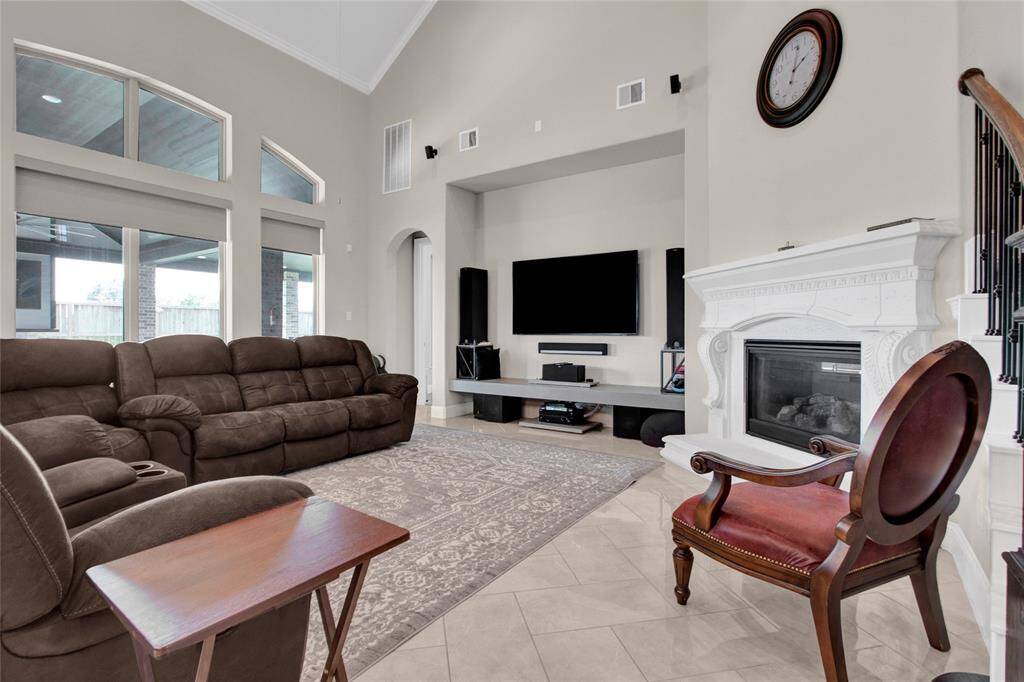 This room features a stunning white cast stone fireplace and expansive windows that brighten the space with natural light, offering lovely views of the covered patio and backyard.