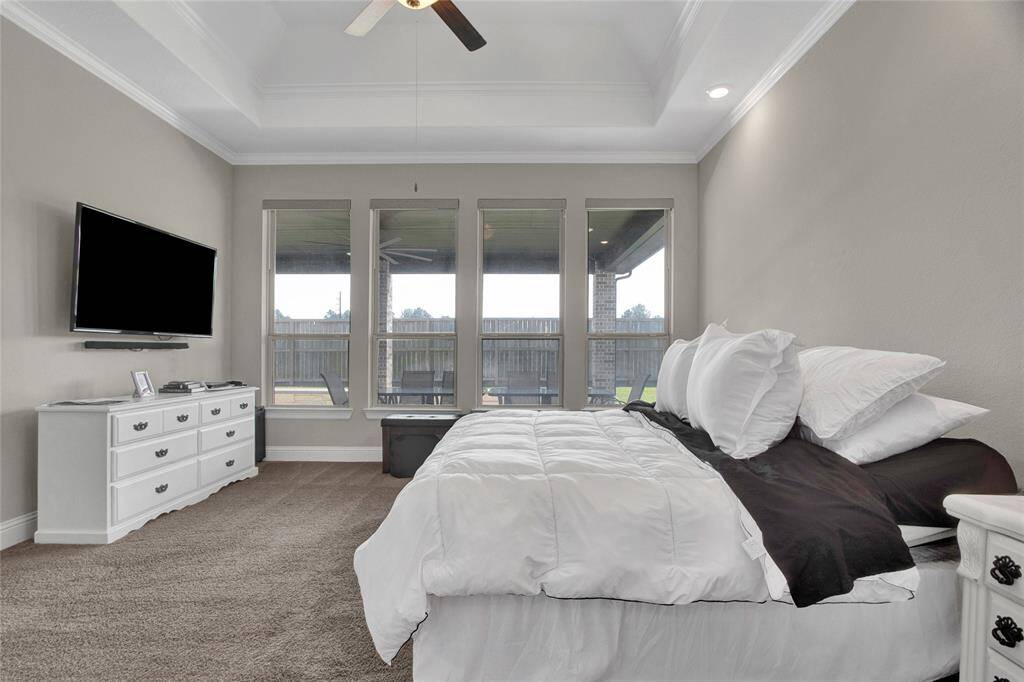 This elegant room features a striking tray ceiling and crown molding, enhanced by large windows that flood the space with natural light and offer serene views of the backyard.