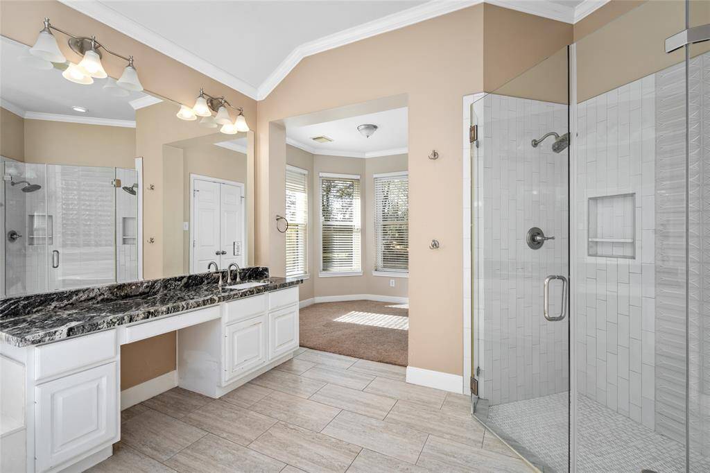 This view highlights the sleek glass shower, offering a modern touch to the primary bath, while also showcasing the extra room that leads into the primary suite. This additional space adds both functionality and style, seamlessly connecting the bath area to the luxurious retreat of the suite.