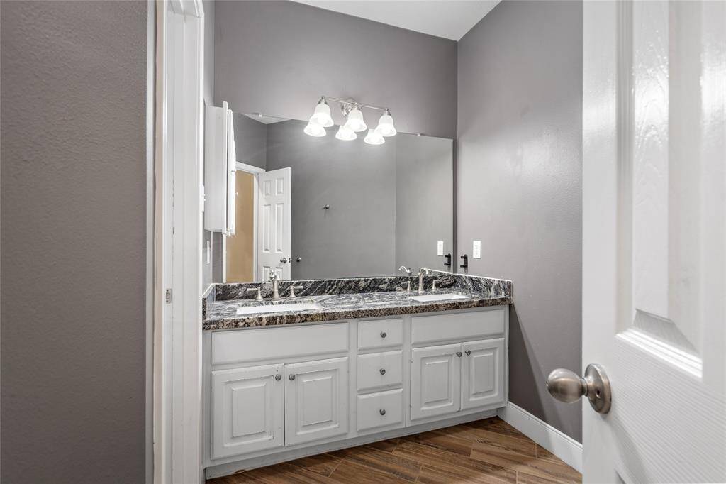 The secondary bathroom features double sinks, providing ample space for convenience and functionality. The frameless window allows for natural light to fill the space, while the soft grey-toned walls create a warm, inviting atmosphere that adds a touch of modern elegance.