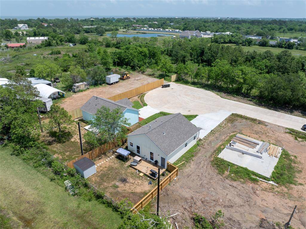This property features a single-story house with a spacious yard, partially fenced, and surrounded by greenery. It offers ample outdoor space, a paved driveway, and is situated in a rural, serene setting with distant views of neighboring homes.