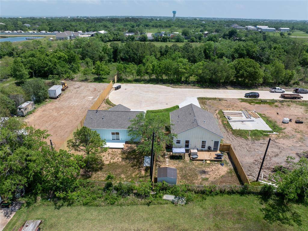 This photo shows a single-story home with a light blue exterior, situated on a spacious lot. The backyard has a small fenced area and a deck. The surrounding area is open and green, providing a sense of privacy and tranquility. Nearby, there are some construction materials, indicating ongoing development.
