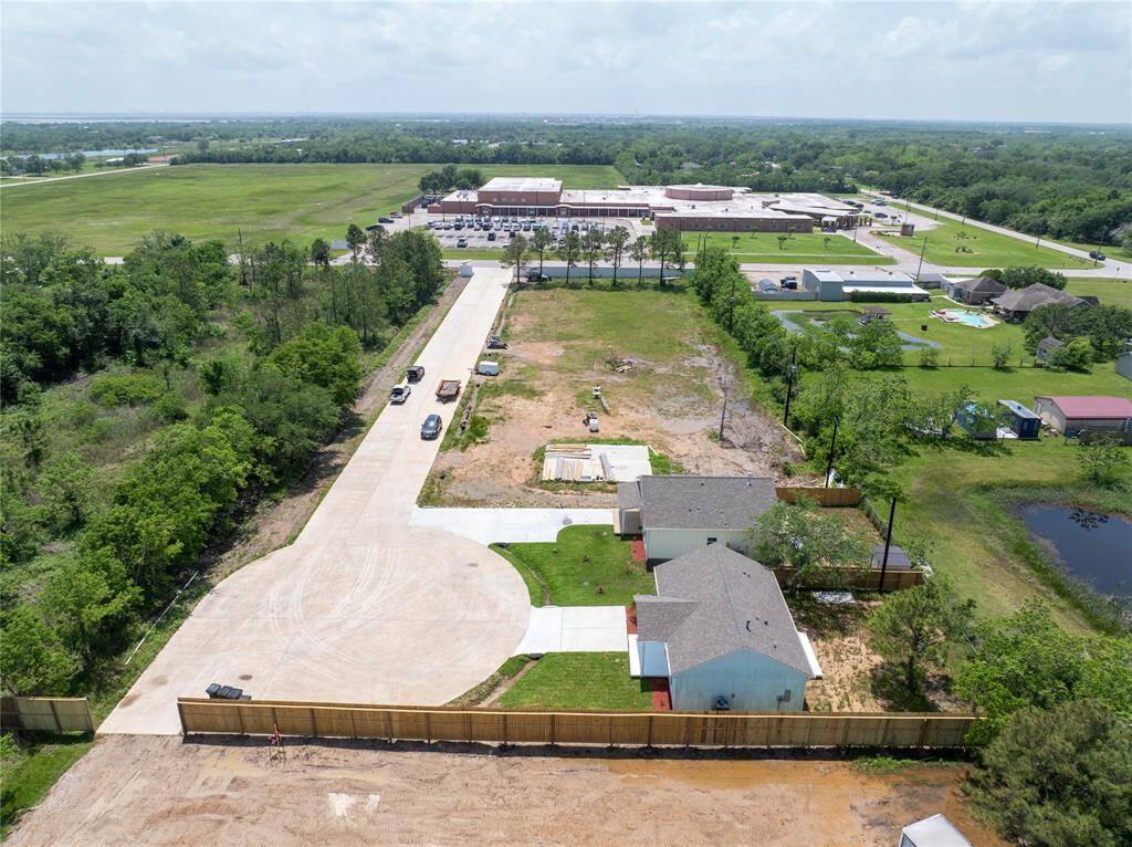 This aerial photo showcases a spacious residential lot with a newly paved driveway leading to a cul-de-sac. The area is bordered by greenery, offering privacy and a serene environment. Nearby, there are some existing homes, an elementary school, and community amenities, providing convenience and accessibility.