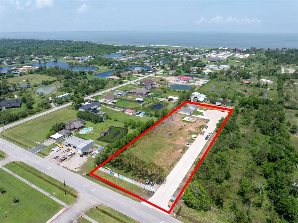 This aerial photo shows a spacious, rectangular plot of land outlined in red, with 8 residential lots and 8 more residential lots on the other side of the cul-de-sac. It's situated in a peaceful, green neighborhood with nearby homes and coastal waterfront.