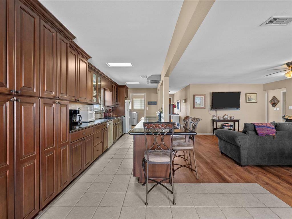Spacious open-concept kitchen and living area featuring rich wooden cabinetry, modern appliances, and a breakfast bar. The living space includes a comfortable seating area with a wall-mounted TV and warm wood flooring, creating a cozy yet functional atmosphere.
