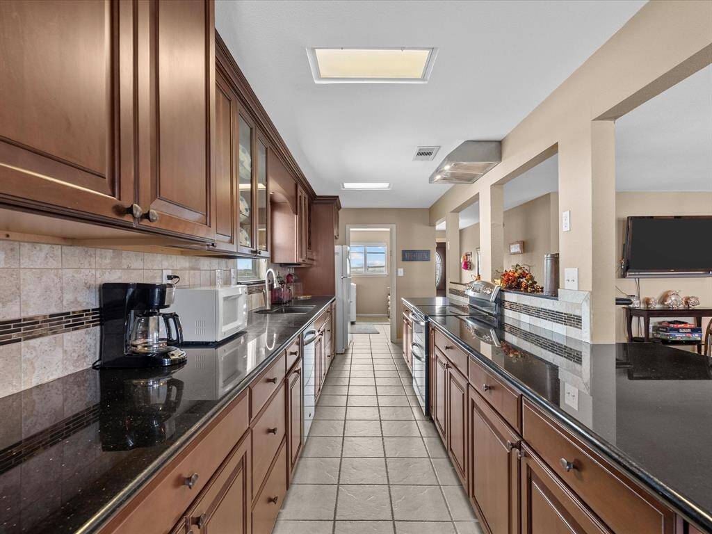 This kitchen features a sleek galley design with dark wood cabinetry and black granite countertops. It includes modern appliances and ample storage, with a tiled floor and open access to adjacent living spaces.