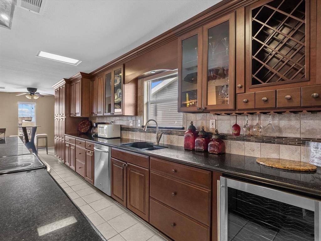 This kitchen features elegant dark wood cabinetry with glass accents and a wine rack, complemented by sleek black countertops. It includes modern stainless steel appliances, ample storage, and a connected dining area with natural light, creating a warm and functional space.