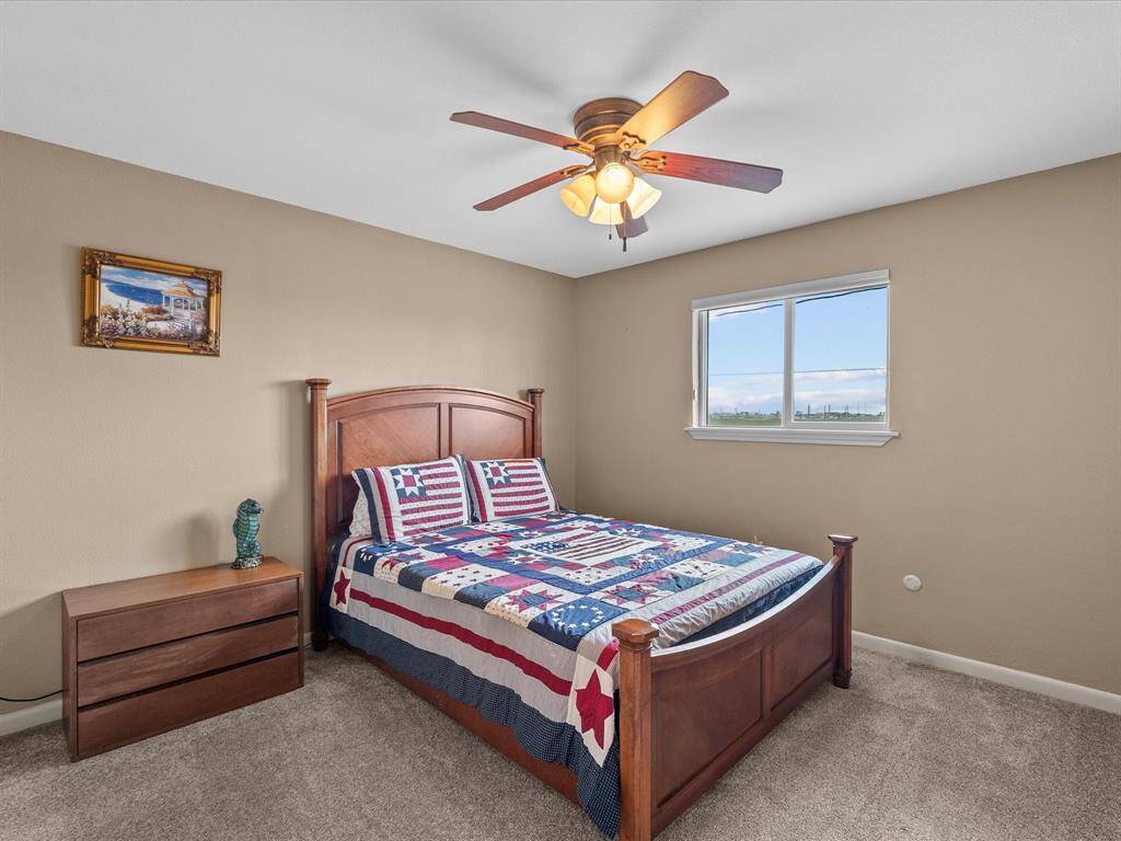 Cozy bedroom with a wooden bed frame, quilted bedding, and a matching nightstand. Features a ceiling fan and a window with a view, offering plenty of natural light.