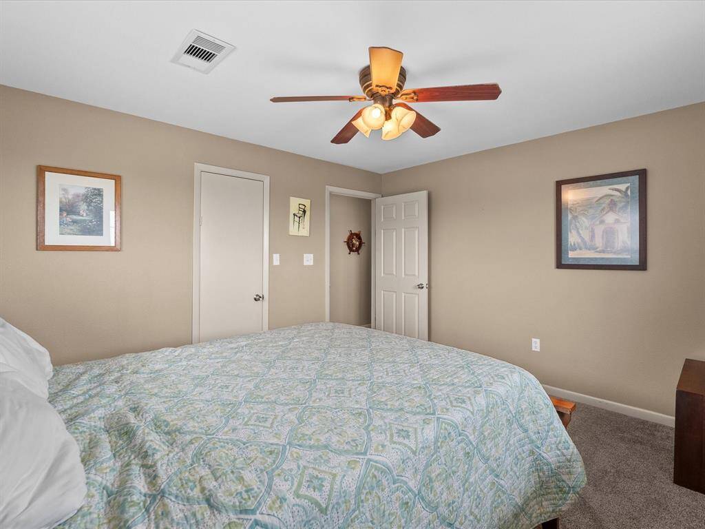This bedroom features neutral walls and carpet, a ceiling fan with lights, and framed artwork. It offers a cozy atmosphere with a large bed and ample space.