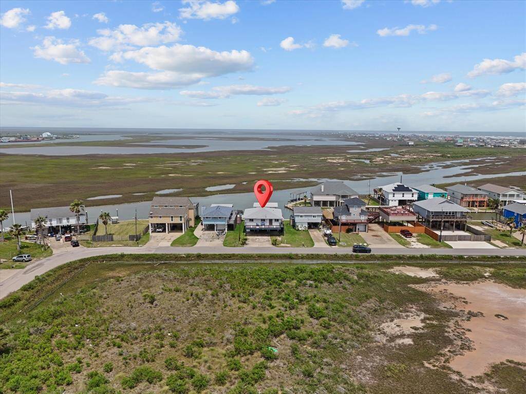 This elevated home features a spacious front deck and twin garages beneath. It's set on a grassy lot with a wide driveway, perfect for parking. The exterior is well-maintained, offering a charming and practical layout for coastal living.