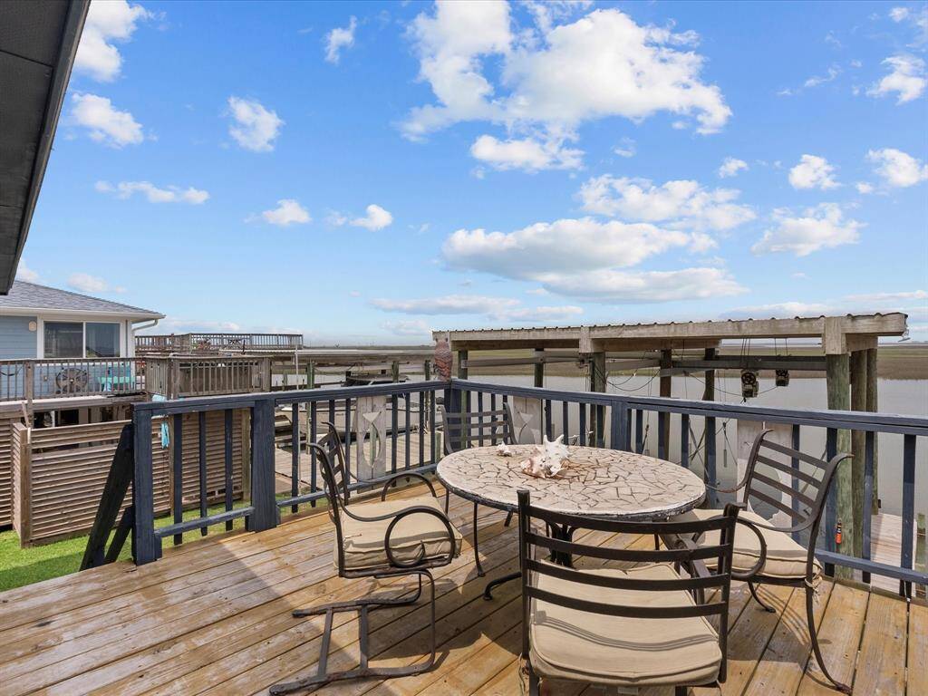This photo showcases a waterfront deck with a round table and chairs, perfect for outdoor dining and relaxing. The view overlooks a serene body of water with neighboring docks, creating a peaceful and inviting atmosphere.