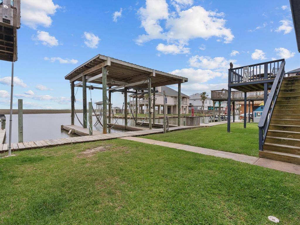 This waterfront property features a wooden dock with a covered boat lift, grassy lawn, and an elevated deck for enjoying scenic water views. Ideal for boating enthusiasts and outdoor relaxation.