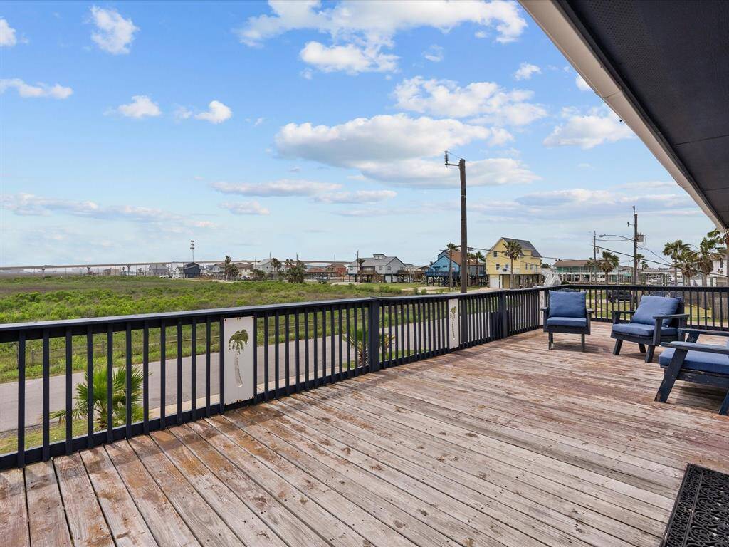 Spacious wooden deck with seating, offering a scenic view of nearby homes and lush greenery under a bright, partly cloudy sky. Ideal for relaxation and outdoor enjoyment.