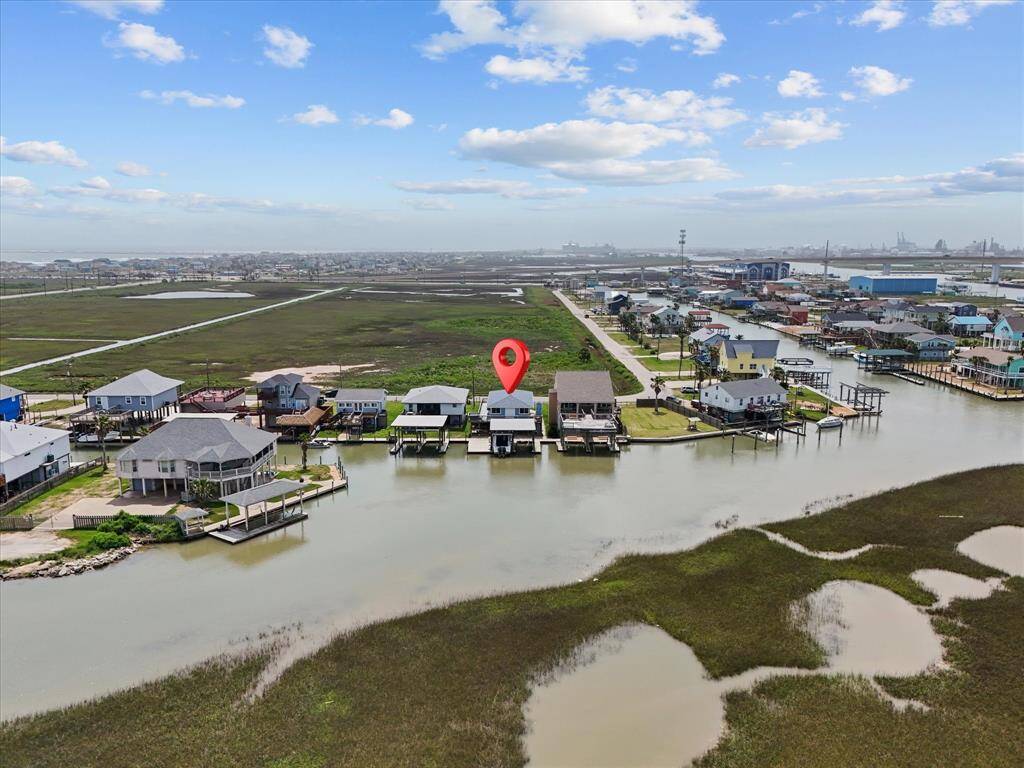 This photo shows a row of homes with a highlighted property, situated near marshlands and water front. The area appears serene, with open green spaces and a clear sky, suggesting a peaceful, coastal living environment.