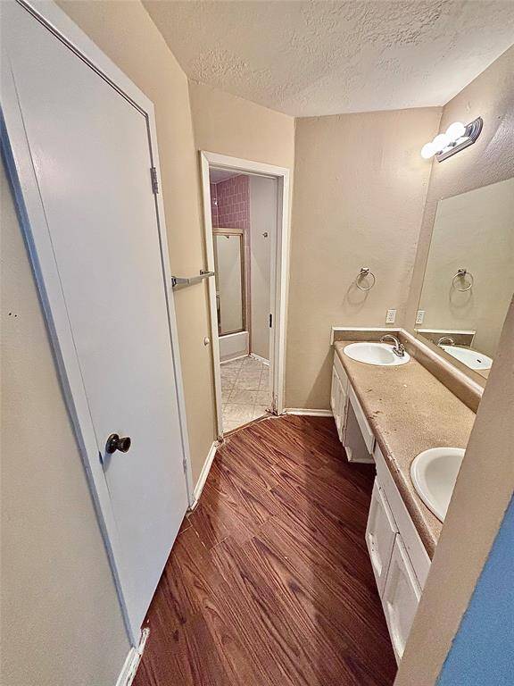 The primary bathroom features dual sinks with a spacious countertop, a large mirror, and wood-style flooring. It leads to a shower area with tile flooring and a glass door.