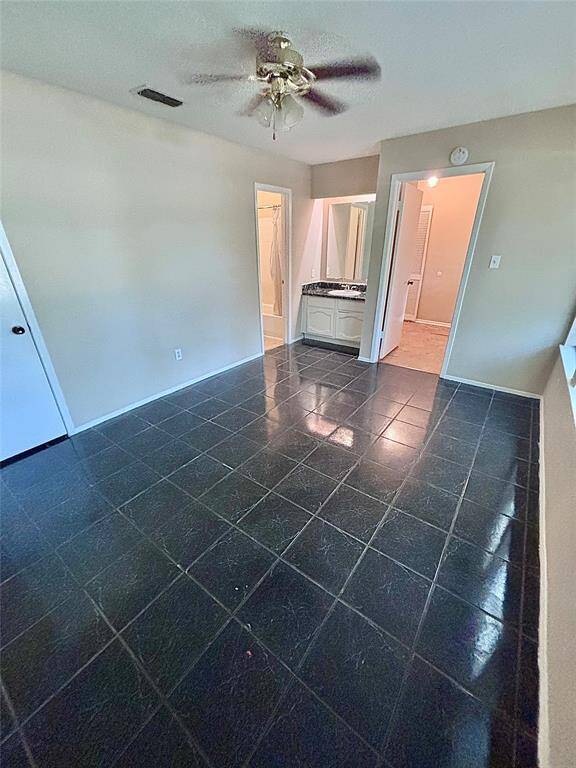 The front bedroom features dark tile flooring and a ceiling fan, with access to the bathroom area that includes a vanity and a tub/shower. The space is bright with ample natural light.
