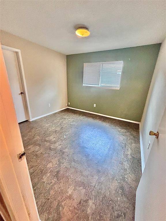 The back bedroom with neutral walls and a green accent wall. It has a window with blinds, a ceiling light, and a door, making it versatile for various purposes.
